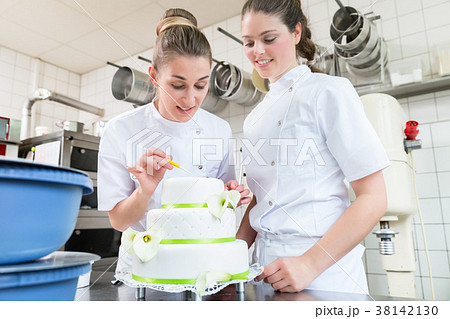 Two pastry bakers decorating large cake 38142130