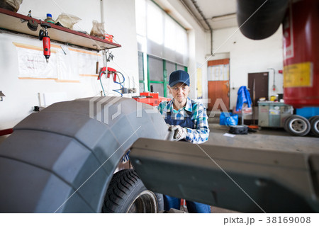 Senior female mechanic repairing a car in a garage Senior female mechanic repairing a car in a garage 38169008