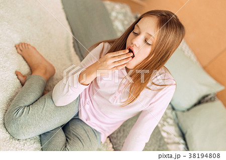 Pleasant teenage girl sitting on bed and yawning Pleasant teenage girl sitting on bed and yawning 38194808