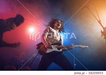 Rock band performs on stage. Guitarist, bass guitar and drums. 38209955