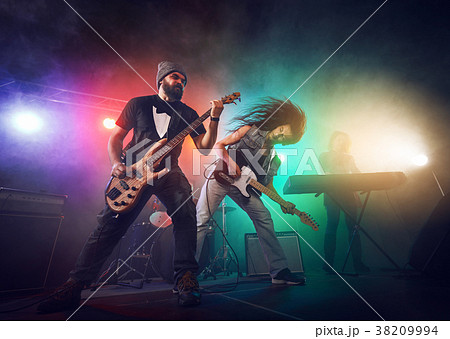 Rock band performs on stage. Guitarist, bass guitar and drums. 38209994