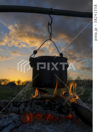 Black pot heating over fire against sunset . Black pot heating over fire against sunset . 38241558