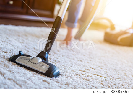 Woman using a vacuum cleaner while cleaning carpet Woman using a vacuum cleaner while cleaning carpet 38305365