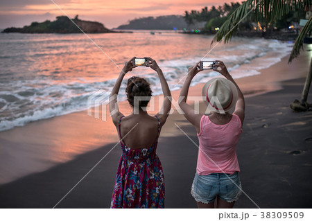 Girls photographing sunset on beach 38309509