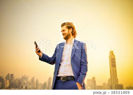 Western businessman using a phone on a rooftop with blurry city Western businessman using a phone on a rooftop with blurry city 38331909