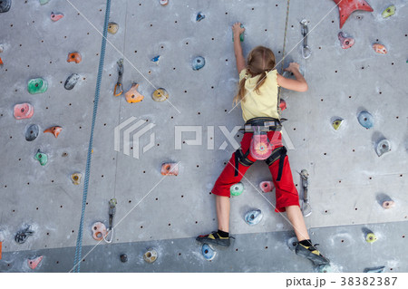 little girl climbing a rock wall indoor. 38382387