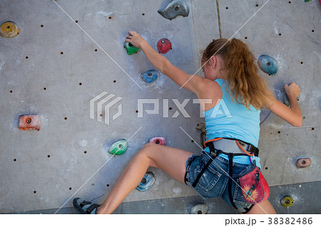 Teen girl climbing a rock wall indoor. Teen girl climbing a rock wall indoor. 38382486
