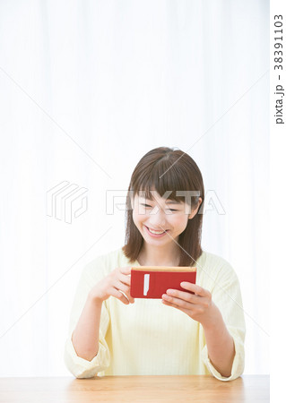 スマホを使う若い女性 女性ポートレート 笑顔 白い家 おしゃれな家 白い背景と女性の写真素材