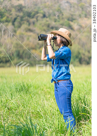 Woman wear hat and hold binocular in grass field Woman wear hat and hold binocular in grass field 38402103