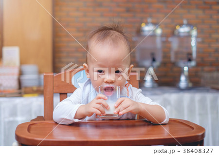 Toddler in high chair drinking milk in a glass 38408327