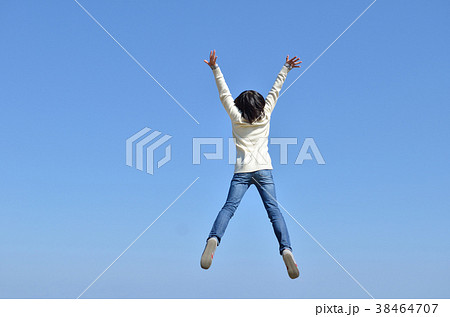 青空でジャンプする女の子 後姿 の写真素材