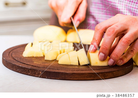 Female hands cut potatoes on wooden board Female hands cut potatoes on wooden board 38486357