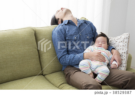 赤ちゃんを抱いて寝落ちするパパの写真素材