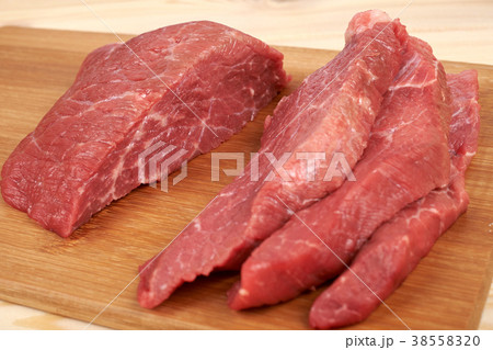 Raw beef piece and slices on wooden cutting board 38558320