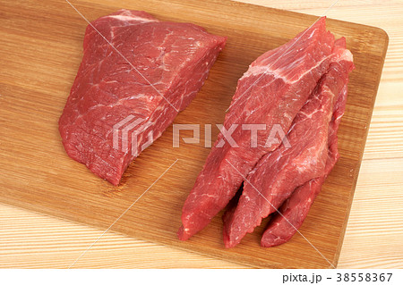 Raw beef piece and slices on wooden cutting board Raw beef piece and slices on wooden cutting board 38558367