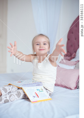 Little blonde girl sitting on the bed reading a Little blonde girl sitting on the bed reading a 38566111
