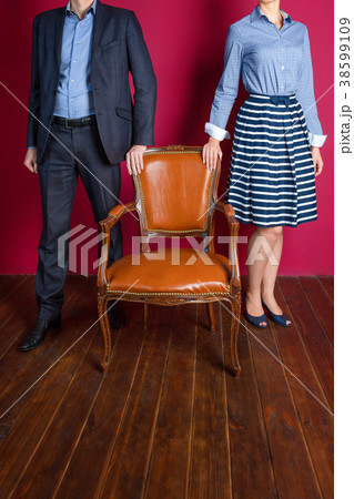 Man and woman standing around empty armchair. Man and woman standing around empty armchair. 38599109