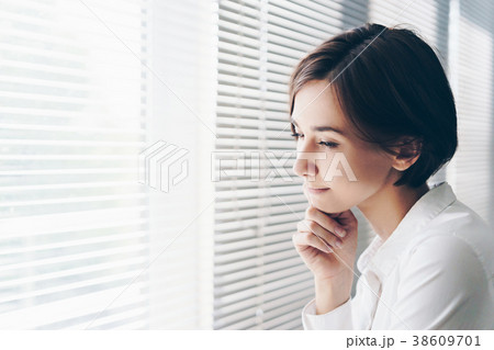 窓のブラインドから外を見つめる女性 38609701