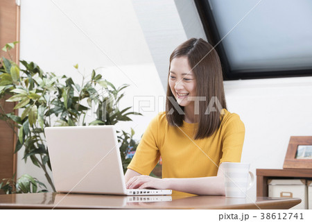自宅のリビングで笑顔でパソコンをする若い女性の写真素材