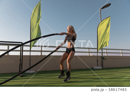 Sports woman doing battle ropes exercises in a 38617483
