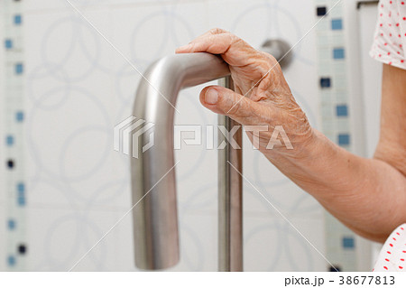 Elderly woman holding on handrail in toilet. 38677813