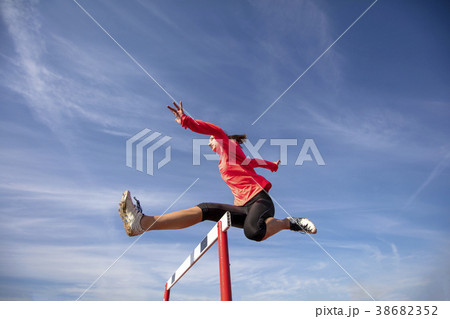 Female athlete jumping above the hurdle during the 38682352