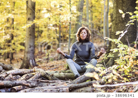 Senior woman meditating in an autumn forest. Senior woman meditating in an autumn forest. 38696341