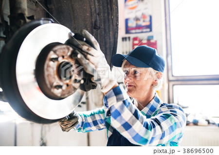 Senior female mechanic repairing a car in a garage Senior female mechanic repairing a car in a garage 38696500
