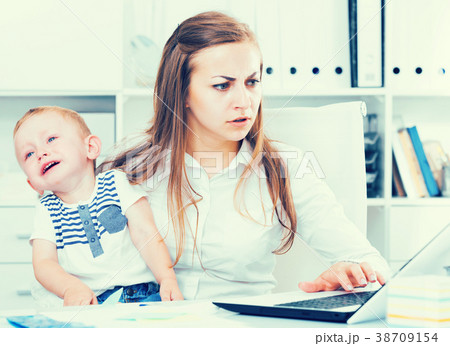 Girl is working with a naughty child in her arms behind a laptop Girl is working with a naughty child in her arms behind a laptop 38709154