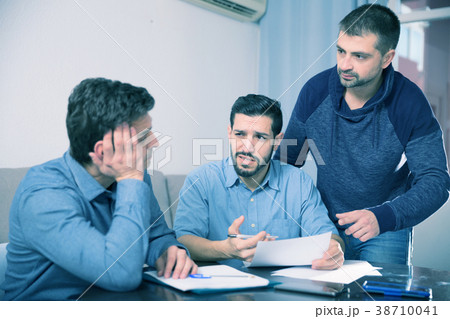 Three troubled men discussing documents at desk Three troubled men discussing documents at desk 38710041