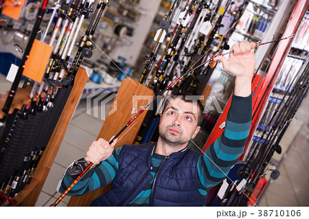 Young male customer standing with fishing rod in shop Young male customer standing with fishing rod in shop 38710106