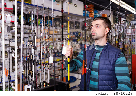 concentrated male choosing fishing rod for fishing in the sports shop concentrated male choosing fishing rod for fishing in the sports shop 38710225