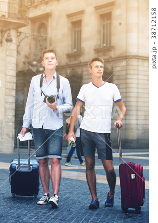 Two positive men in shorts with luggage walking 38712158