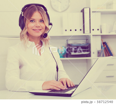 Young call center employee in headphones is sitting near laptop in the office Young call center employee in headphones is sitting near laptop in the office 38712540