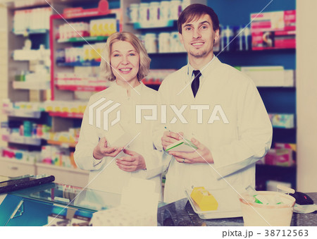 Pharmacist and pharmacy technician posing in drugstore Pharmacist and pharmacy technician posing in drugstore 38712563