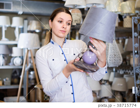 Girl is choosing modern table lamp in furniture store. Girl is choosing modern table lamp in furniture store. 38715774