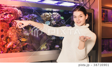 Young smiling girl near big aquarium is pointing to interesting 38716901