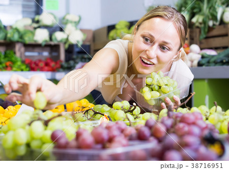 cheerful young woman seller holding bunch of grapes on market 38716951