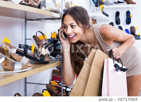 portrait of woman chatting on phone while picking new shoes in store 38717064