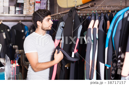 man holding and choosing suit for surfing in the shop 38717157