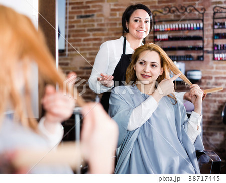Woman points to master in hairdress salon right hair length for haircut Woman points to master in hairdress salon right hair length for haircut 38717445
