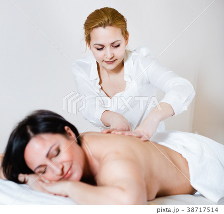 Young massagist doing shoulder massage to adult woman 38717514