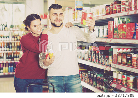 Happy couple choosing purchasing canned food for week at supermarket Happy couple choosing purchasing canned food for week at supermarket 38717889