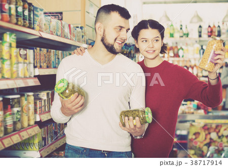Couple standing near shelves with canned goods at store Couple standing near shelves with canned goods at store 38717914