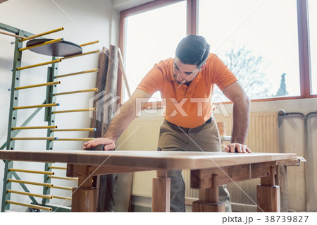 Carpenter polishing and varnishing a table 38739827
