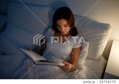 young woman reading book in bed at night home young woman reading book in bed at night home 38749170
