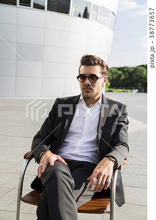 Man in suit sitting on chair near modern building Man in suit sitting on chair near modern building 38773657