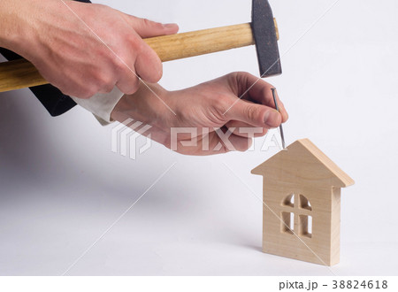 Man hammers a nail in a miniature wooden house Man hammers a nail in a miniature wooden house 38824618