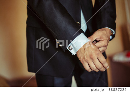 The man fastens the cuffs of his shirt. 38827225