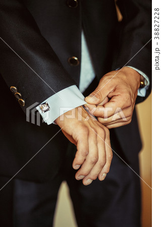 The man fastens the cuffs of his shirt. 38827228